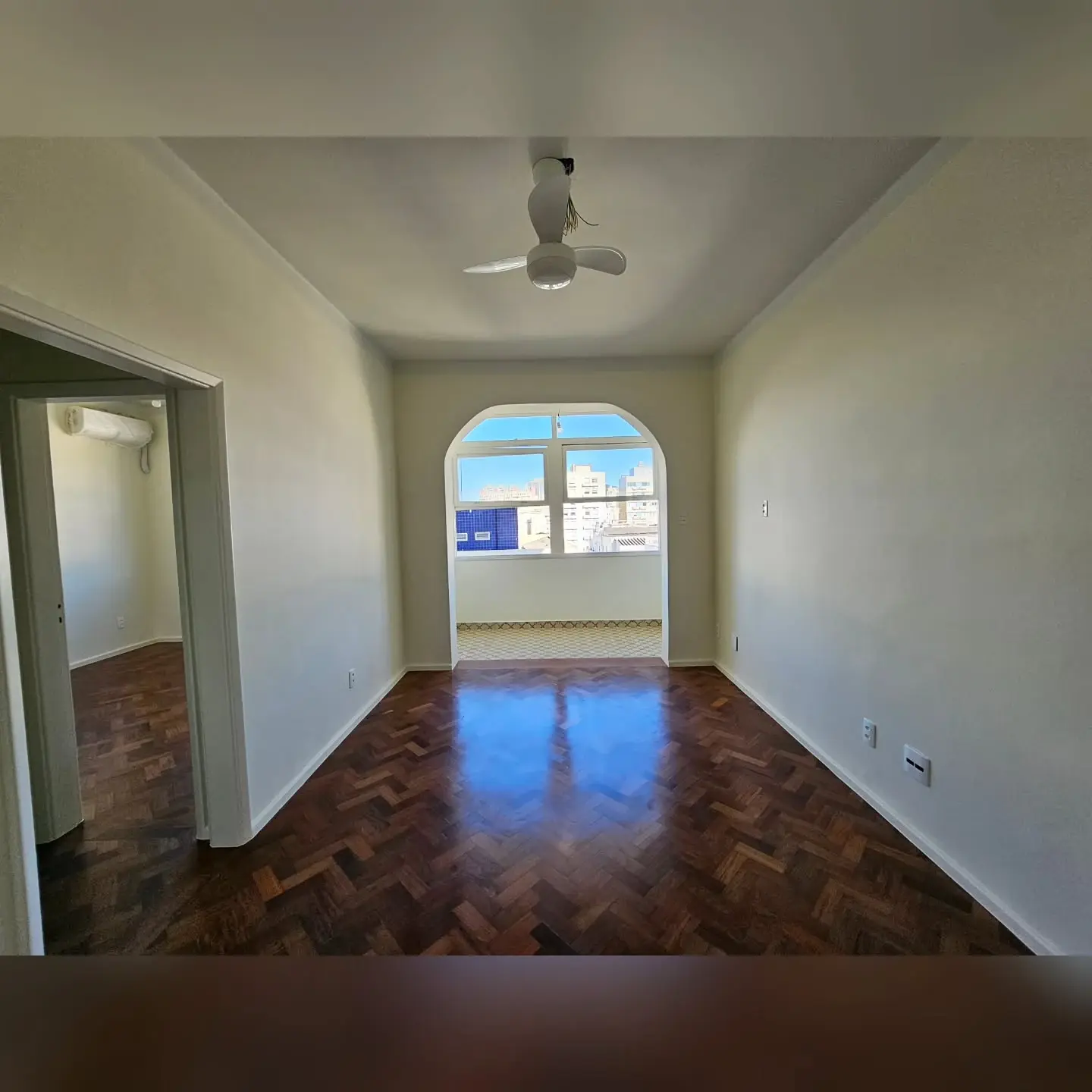 Sala após a reforma, com paredes claras, piso de madeira e passagem em arco para a varanda