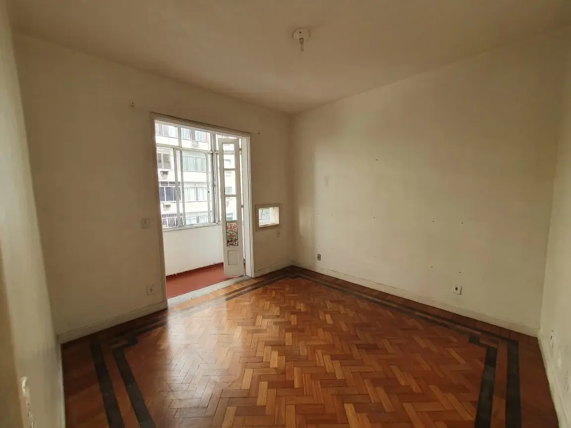 Quarto antes da obra, vazio, com piso de tacos de madeira, porta de varanda e paredes claras